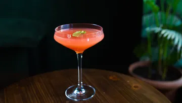 Pinkfarbener Cocktail im Glas auf Holztisch.