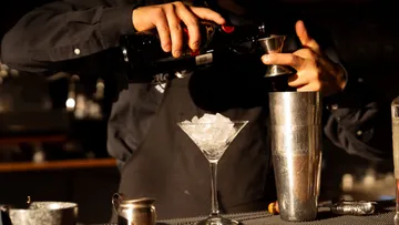 Barkeeper gießt Likör in Shaker an Bar.