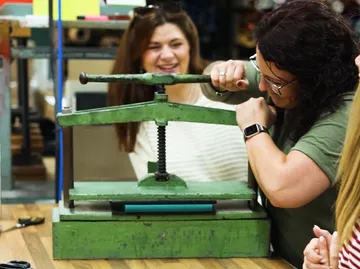 Woman operates green press, others watch closely.