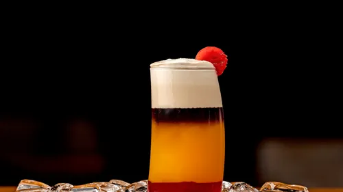 Layered cocktail with a cherry garnish on ice.