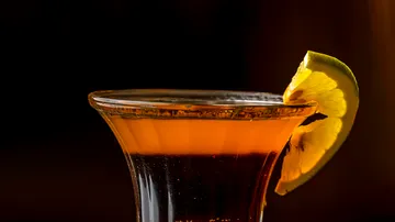 Orange cocktail with lemon garnish, dark backdrop.