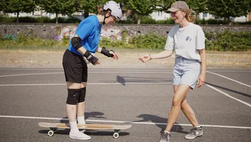 Two women skateboarding in a sunny park.