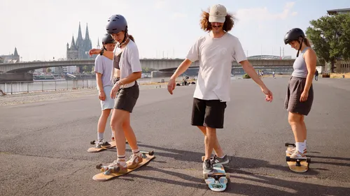 Four people skateboarding near a bridge.