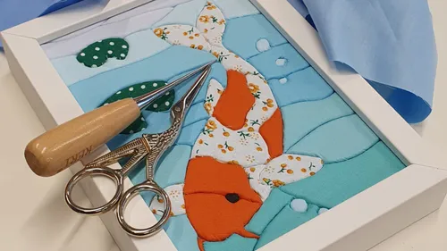 Fabric koi fish, framed, with scissors nearby.