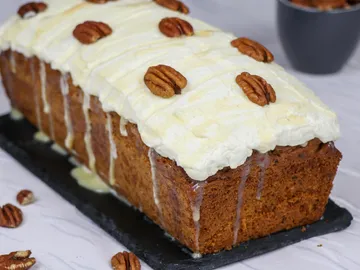 Ein Kuchen liegt auf einem schwarzen Brett, garniert mit Nüssen.