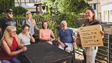 Group sitting outside, woman holding sign.
