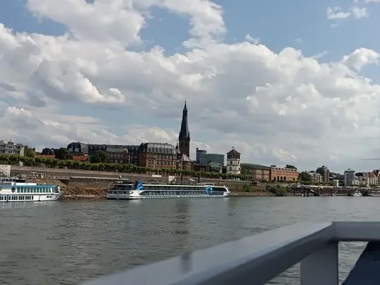Stadtansicht mit Flussschiffen und Kirchturm.