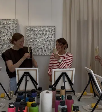 Personen stoßen in Kunstkurs mit Staffeleien an.