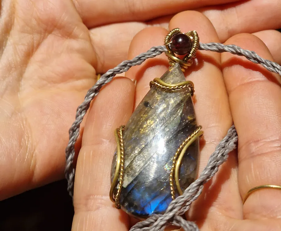 Pendant held in hands, intricate wire wrapping.