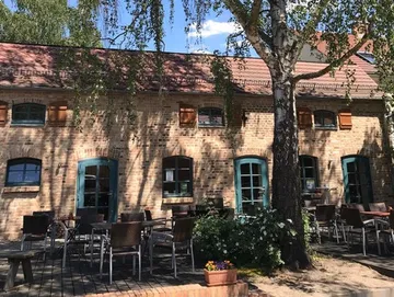 Historisches Gebäude mit Tischen im Freien unter Bäumen.