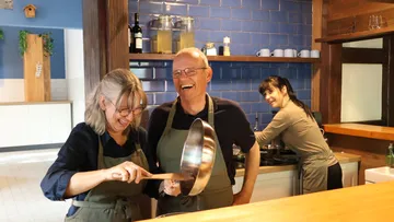 Three people cooking and laughing in kitchen.