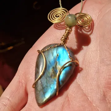 Blue stone pendant with gold wire on hand.