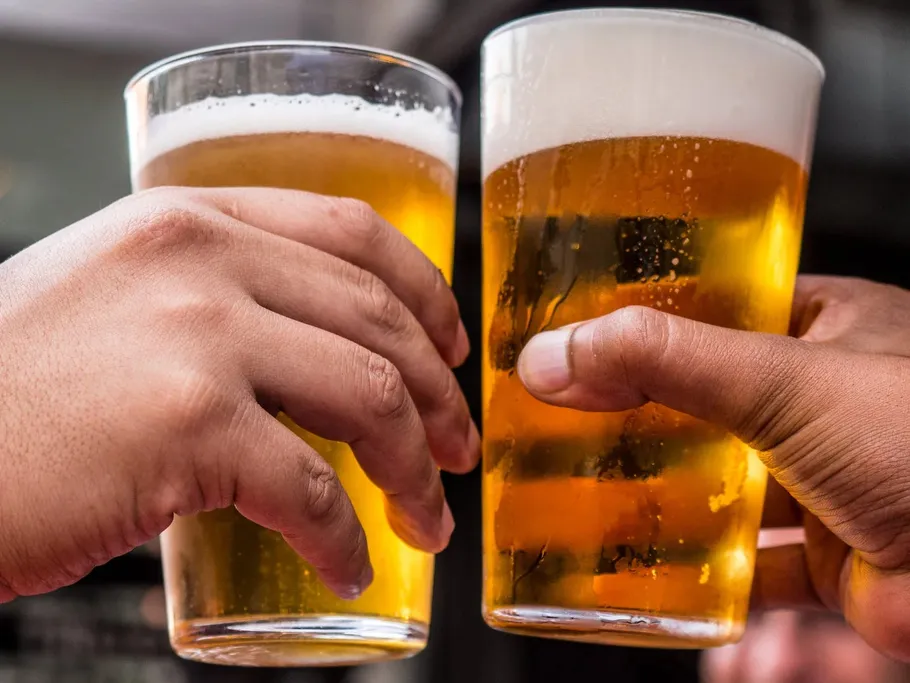 Two hands bump glasses of beer together in a cheerful atmosphere.