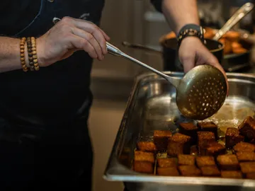 Cook scoops fried cubes from a stainless steel plate.
