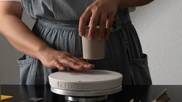 Person formt Keramikbecher auf Töpferscheibe.