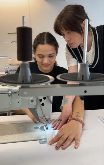 Zwei Frauen nähen mit Maschine in Werkstatt.
