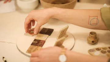Hand arranging tiles on circular board, desk setting.