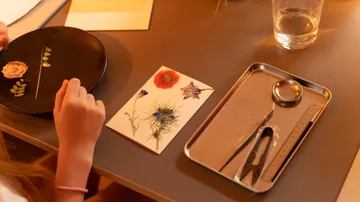 Child crafting with pressed flowers on table.