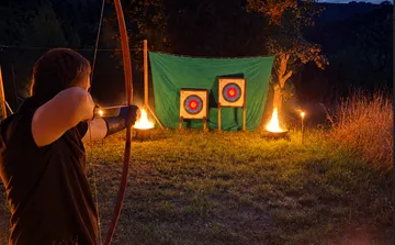 Bogenschütze zielt auf Ziele im Freien bei Nacht.
