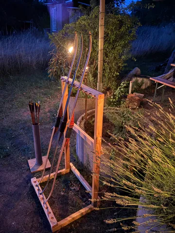 Bows on stand near torchlight, outdoors.