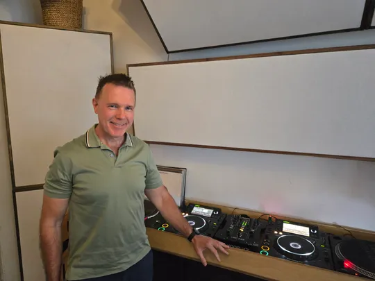 Mann steht neben DJ-Ausrüstung im Raum.