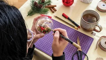 Person bastelt Weihnachtsdekoration am Tisch.
