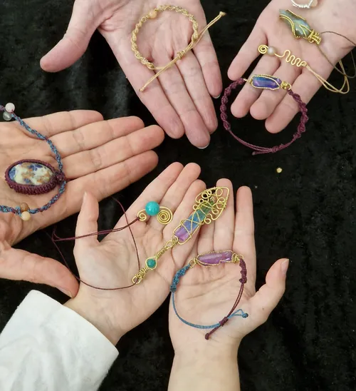 Hände zeigen handgefertigten Schmuck auf schwarzem Untergrund.
