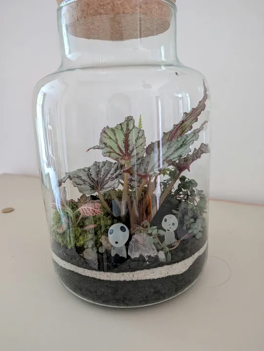 Glass jar containing plants and decorative figures.
