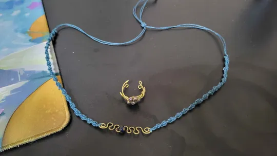 Blaue Halskette und goldener Ring auf Tisch.