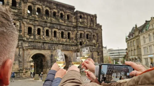 Hände halten Weingläser vor antikem Steingebäude.