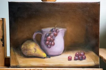 Pear and grapes beside a jug on table.