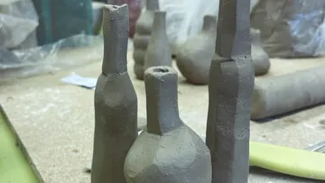 Clay bottles shaped on a workbench.