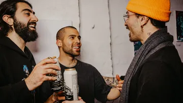 Three men chatting, holding drinks indoors.
