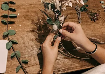 Hände binden Trockenblumen auf einem Holztisch zusammen.