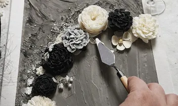 Hand using palette knife on floral artwork.