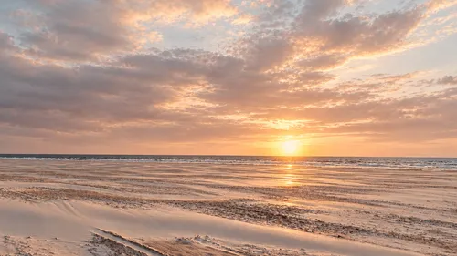 Sun setting over calm beach and ocean.