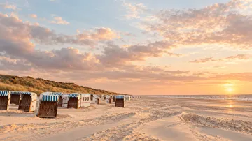 Beach chairs facing sunset on sandy beach.