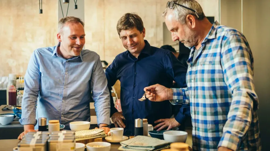 Three men tasting coffee in kitchen.
