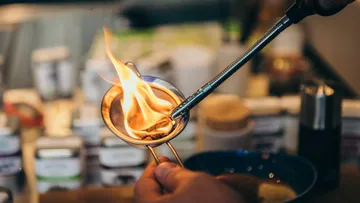 Hand torching strainer with flames in kitchen.