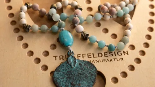 Beaded necklace with leaf pendant on wood.