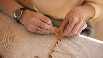 Hands creating beaded jewelry on fabric.