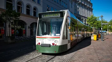 Tram moving down city street in daylight.