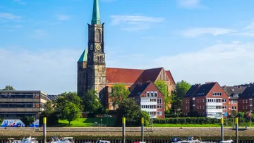 Kirche mit Turm am Fluss, klarer Himmel.