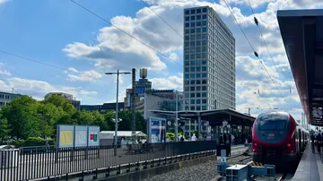 Zug erreicht städtischen Bahnhof mit Hochhaus.