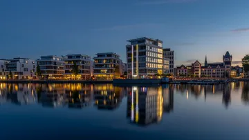 Gebäude spiegeln sich im ruhigen Abendwasser.
