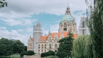 Historisches Gebäude mit Gerüst, umgeben von Grün.
