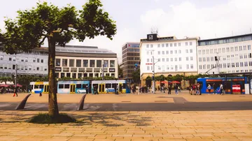 Tram passing through city square with buildings.