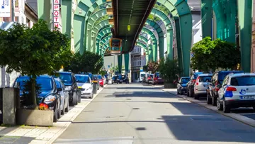 Schwebebahn fährt über von Autos gesäumte Straße.