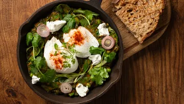 Skillet with poached eggs, herbs, bread nearby.