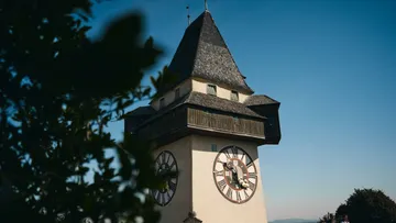 Uhrturm mit Laub, klarer Himmel.